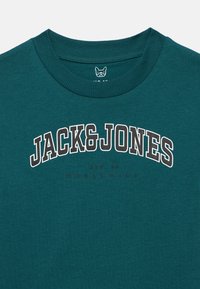 Τυρκουάζ κοντομάνικο μπλουζάκι με στρογγυλή λαιμόκοψη, με το λογότυπο "JACK&JONES" σε έντονα λευκά και γκρι γράμματα, και το "EST. 90" σε μικρότερο κόκκινο γράψιμο από κάτω.