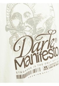 Bijela pamučna majica s detaljnim grafičkim printom dizajna sunca i orla, s natpisom "Tamni Manifest" u tamnosmeđoj boji.