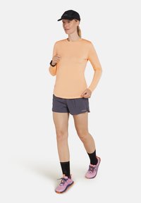 Ljusorange långärmad tröja, grå shorts, svarta strumpor, rosa och orange sportskor, svart keps. Fokus på design och färger av aktivkläder.