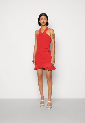 Vestido vermelho com alça no pescoço apresentando uma silhueta ajustada, barra com babados e textura suave, complementado por sandálias prateadas com tiras.