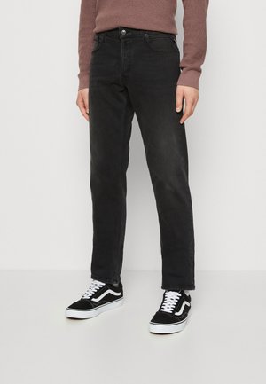 Črne jeans hlače z ravnim krojem, ki vključujejo pet žepov in subtilno zbledelost. Kombinirane s črnimi in belimi športnimi copati.