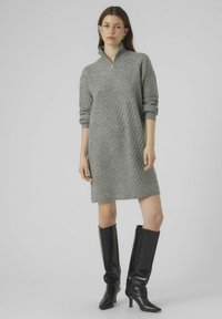 Abito grigio lavorato a maglia con un motivo a zigzag testurizzato, colletto alto con zip e maniche a tre quarti, abbinato a stivali neri in pelle verniciata al ginocchio.