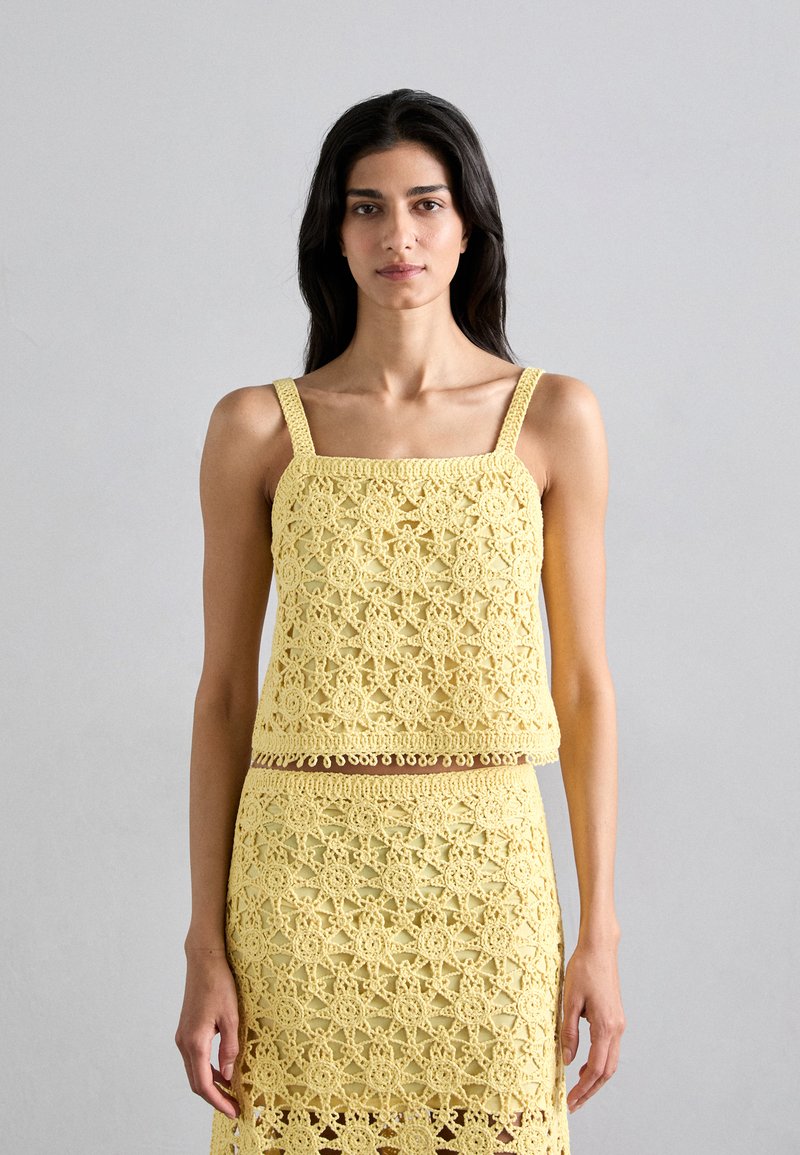 Haut au crochet jaune avec encolure carrée et bretelles larges, doté de motifs floraux et d'un ourlet festonné, associé à une jupe assortie.
