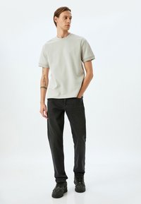 Lys grå kortærmet t-shirt med rund hals, kombineret med sorte lige ben jeans og mørke sneakers med en struktureret overflade.