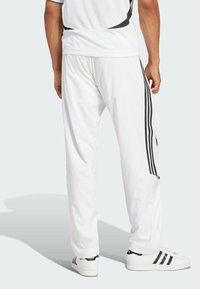 Fehér sportnadrág fekete Adidas csíkokkal az oldalán, sima, könnyű anyagból készült. Zsebekkel rendelkezik és laza fazonú az alsó része.