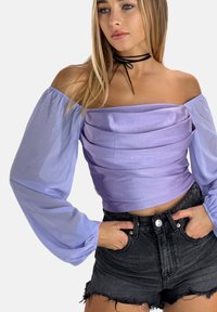 Lavendel off-shoulder top med samling detaljer og gennemsigtige puffærmer, parret med højtaljede sorte denimshorts.