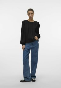 Sort ribbet langærmet top med puffede skuldre, parret med lys blå brede jeans og sorte sko med hvid detalje.