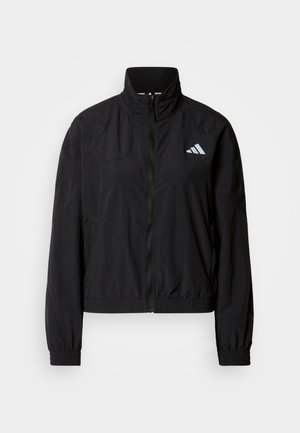 Sort vindjakke med høj krave, lynlås foran og elastiske ærmekanter. Har en reflekterende logo på øverste venstre side. Letvægtsmateriale.