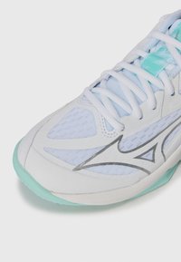 White athletic shoe with a mesh upper, light blue accents, silver logo, and a mint green sole. Features laces and textured materials.