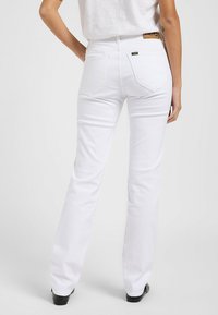 Jeans de mezclilla blancos acampanados con un diseño de bolsillo trasero y parche de cuero de la marca, que presentan una textura suave y una cintura ajustada.