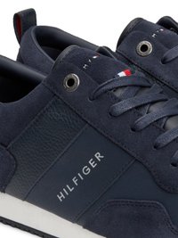 Sapatilhas azul-marinho em materiais de camurça e pele, com atacadores cinzentos, uma entressola branca e um logo impresso "HILFIGER" na lateral.