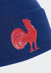 Niebieska dziana czapka z teksturowanym, prążkowanym wzorem. Na przodzie znajduje się wyraźne, czerwone haftowane logo koguta.