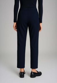 Pantaloni su misura blu navy con una trama liscia, caratterizzati da un design elegante, tasche laterali e gamba dritta, abbinati a scarpe nere senza lacci.