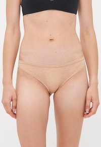 Woman wearing beige low-rise underwear and a black crop top, shown from midriff to mid-thigh against a plain background.