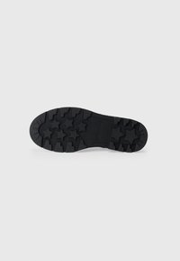Semelle de chaussure en caoutchouc noir avec des crampons en forme d'étoile, des motifs texturés et un design plat, avec un détail en relief rectangulaire.