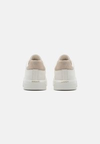Weiße Sneaker mit einem Obermaterial aus glattem Leder, Akzenten aus Wildleder an der Ferse und strukturierten Gummisohlen. Goldenes "GANT"-Logo an der Ferse.
