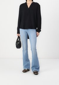 Černý top s dlouhým rukávem a výstřihem do V, modré rozšířené džíny, boty s leopardím potiskem a malá černá kabelka.