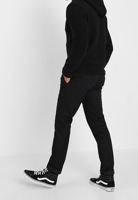 Felpa nera con zip in tessuto testurizzato, pantaloni neri con tasche e sneaker alte nere con dettagli bianchi. Outfit casual.