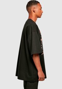 Tricou din bumbac oversize, de culoare neagră, cu mâneci scurte, având un design grafic pe față. Țesătura pare moale, cu o textură netedă.