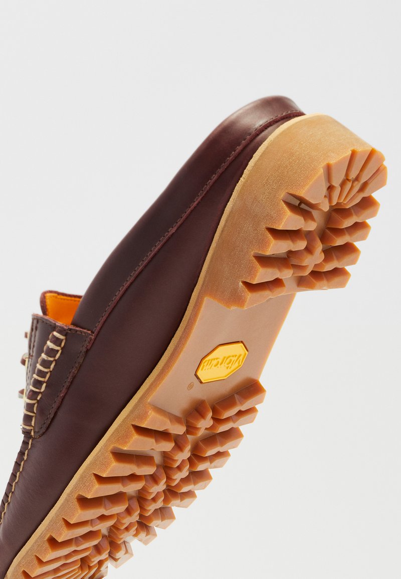 Scarpa in pelle marrone con suola in gomma testurizzata. Presenta un accento cucito e un logo "Vibram" giallo ben visibile alla base della suola.