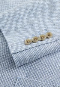 Lichtblauwe blazer met textuur, mouw met vier beige knopen netjes bij de boord.