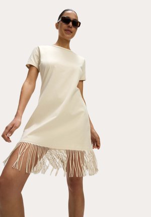 Robe t-shirt de couleur crème à manches courtes, avec un ourlet à franges en tissu doux qui tombe élégamment.