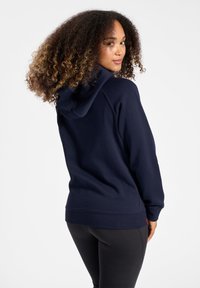 Felpa blu navy realizzata in tessuto morbido, con cappuccio regolabile, polsini e orlo a coste; abbinata a leggings neri.
