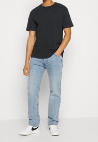 Camiseta de algodón negra con cuello redondo combinada con jeans de mezclilla azul claro. El atuendo se completa con zapatos blancos que tienen un acento negro.