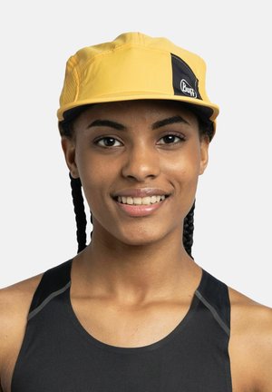 Gorra amarilla con un panel de acento negro y logo, diseñada con una tela ligera, con una corona estructurada y visera, llevada por un modelo.