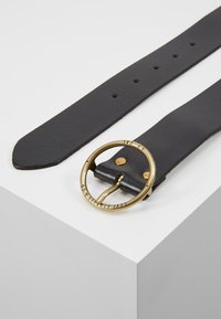 Ceinture en cuir noir avec une texture lisse, dotée d'une boucle ronde en métal doré et de trous visibles pour l'ajustement.