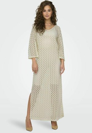 Vestido maxi hecho de tejido de punto abierto de color crema, con mangas tres cuartos, escote en V y aberturas laterales para mayor movimiento.