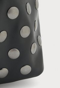 Svart strukturerad lädersyta med stora, jämnt fördelade, runda metallnitar arrangerade i ett rutmönster.
