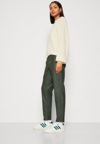 Cremefarvet, ribbet sweater med puffede ærmer, olivengrønne bukser med glat tekstur og hvide sneakers med grønne accenter.