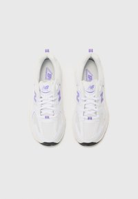 Hvide atletiske sneakers med mesh-overdel, lilla accenter og tyk gummisål. Har snørebånd og branding på tungen.