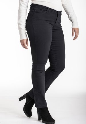 Jeans skinny noirs en denim, avec une taille mi-haute et une texture lisse. Portés avec des bottines à talons hauts noires.