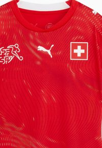 Κόκκινη αθλητική φανέλα από αναπνεύσιμο ύφασμα με υφασμένο κυματιστό σχέδιο, λευκό λογότυπο Puma και έμβλημα της σημαίας της Ελβετίας στο στήθος.