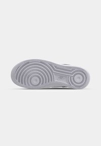 Semelle d’une basket Nike gris clair avec motifs circulaires sur la bande de roulement et logo Nike au centre sur fond blanc.