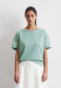 Hellgrünes Baumwoll-T-Shirt mit Rundhalsausschnitt und kurzen Ärmeln, das eine lockere Passform und einen leicht längeren Rückenbund aufweist.