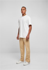 Hvid bomulds t-shirt, løs pasform, parret med beige sweatpants med sidesømme. Bæres med hvide atletiske sneakers. Ensfarvet baggrund.