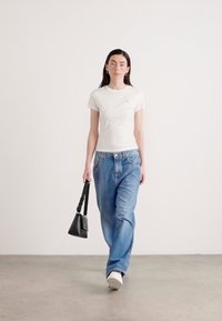 T-shirt bianca aderente, jeans leggeri azzurri larghi e sneaker bianche. Tieni in mano una piccola borsa nera. Tessuto liscio con un design casual.
