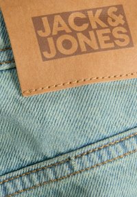 Denim tkanina u svijetloplavoj boji s narančastim šavovima; uključuje smeđu kožnu oznaku s utisnutim logom "JACK & JONES".