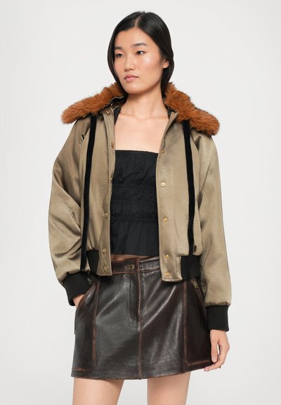 Khaki bomber jacket with faux fur orange collar, black ribbed cuffs, gold snap buttons, worn over a black smocked top and brown leather skirt.