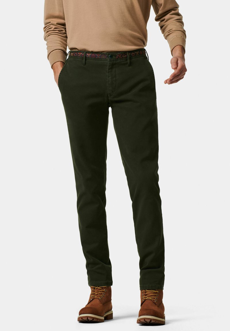 Dunkelgrüne Chinos mit schlanker Passform, versehen mit einem gemusterten Gürtel, glatter Textur und passenden braunen Schnürstiefeln.