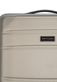 Maleta rígida plateada con superficie texturada, acentos negros y el logo de WITTCHEN. Presenta líneas horizontales y un asa robusta.