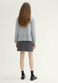 Un pull gris clair avec un ourlet à côtes, associé à une jupe à carreaux noir et blanc. Des chaussures noires et des chaussettes complètent la tenue.