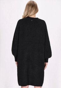 Zwarte gebreide oversized jurk met een gestructureerd ribpatroon, raglanmouwen en een ronde halslijn, die tot halverwege de dij reikt.