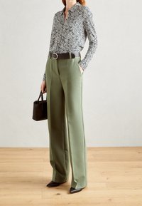 Een zwart-wit gestreepte shirt, olijfgroene high-waisted broek, zwarte riem met een ronde gesp, zwarte handtas, zwarte puntige hakken.