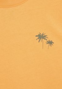 Oranžové bavlnené tričko s jemnou grafikou zelenej palmy na ľavej hrudi. Hladká textura s okrúhlym výstrihom.