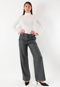 Maglione bianco a collo alto abbinato a pantaloni grigi a quadri a gamba larga e scarpe nere con tacco alto. L'outfit presenta una silhouette aderente e una texture liscia.