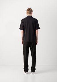 Svart kortermet polo skjorte med rett snitt, kombinert med svarte, løse bukser og hvite sneakers. Jevn stoffoverflate.